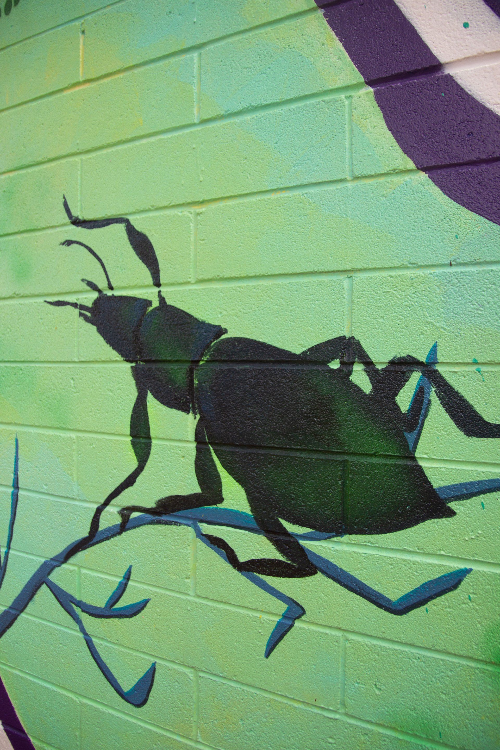 A bug is painted on a green and purple brick wall.