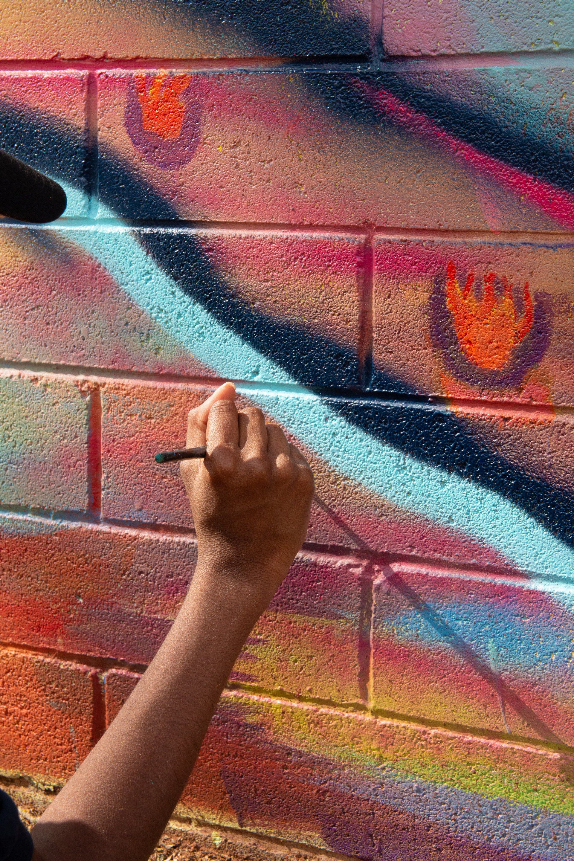 A person is spray painting graffiti on a brick wall.