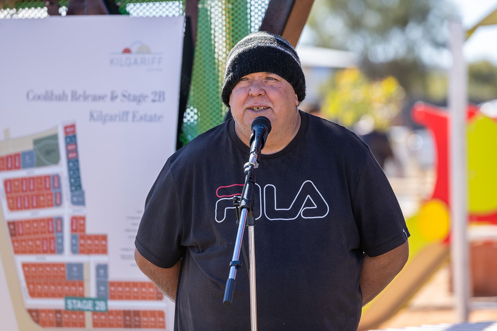 A man wearing a black fila shirt stands in front of a microphone