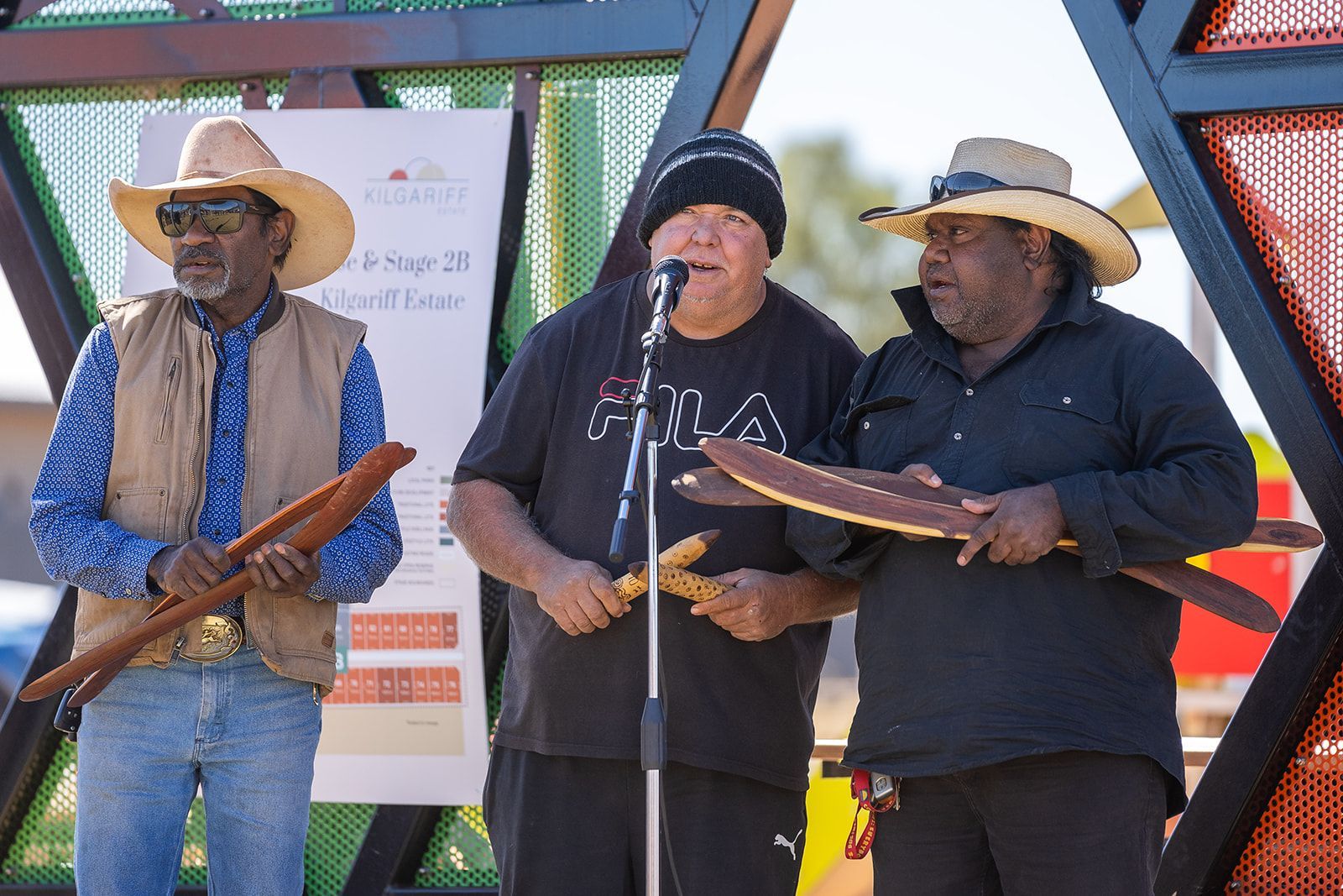 Three men are standing in front of a microphone holding instruments.