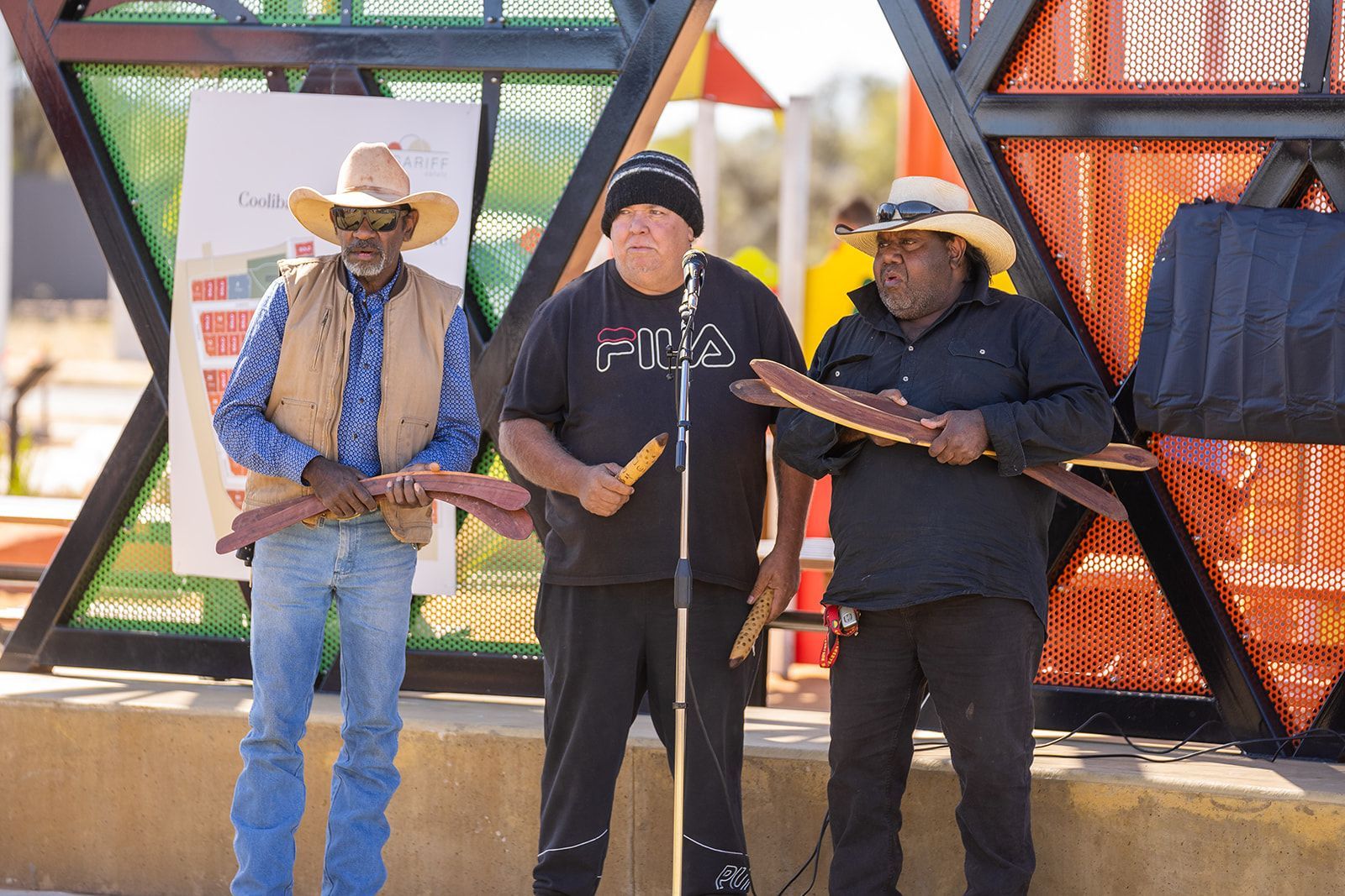 Three men are standing next to each other holding sticks in front of a microphone.