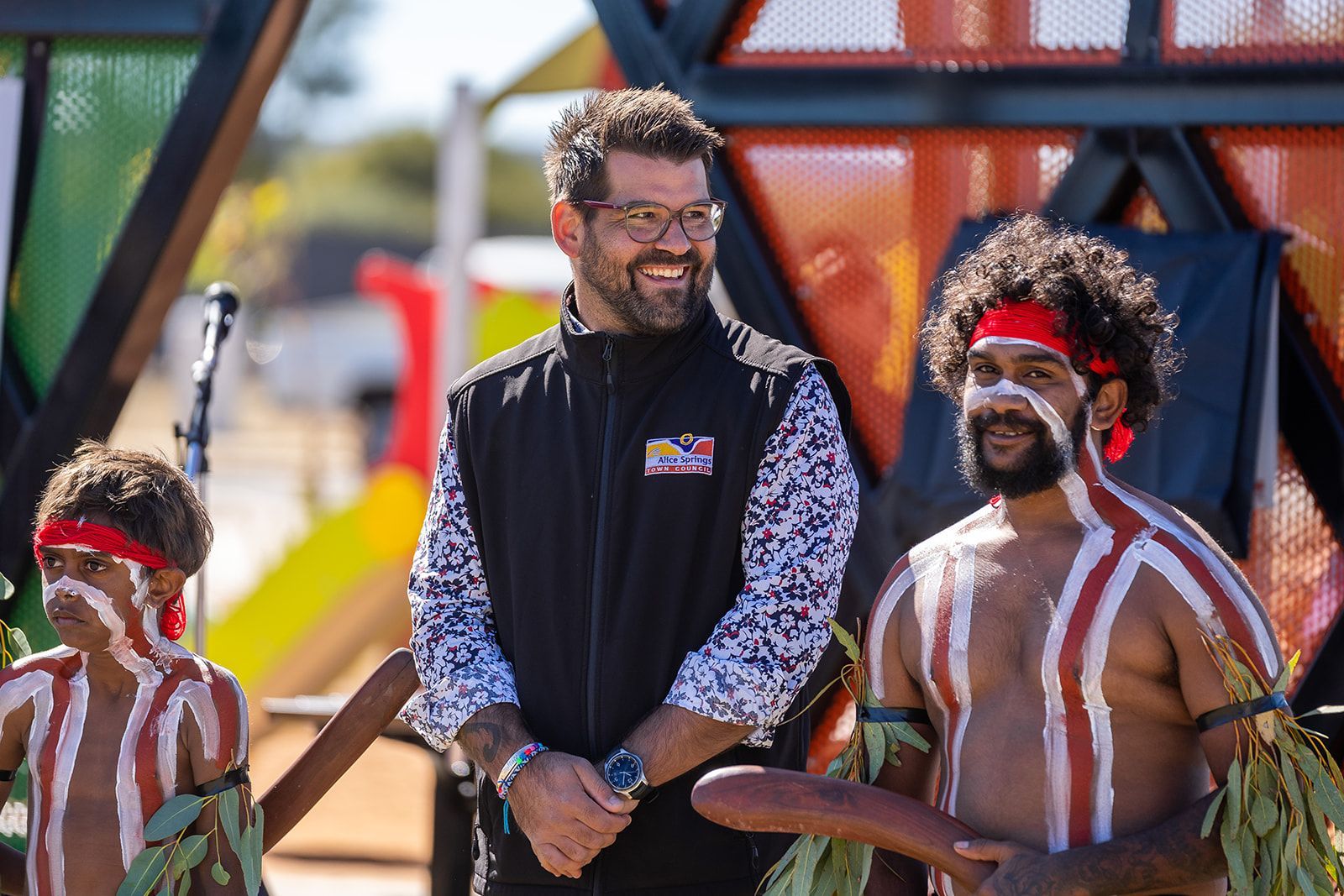 A man is standing next to two aboriginal men.