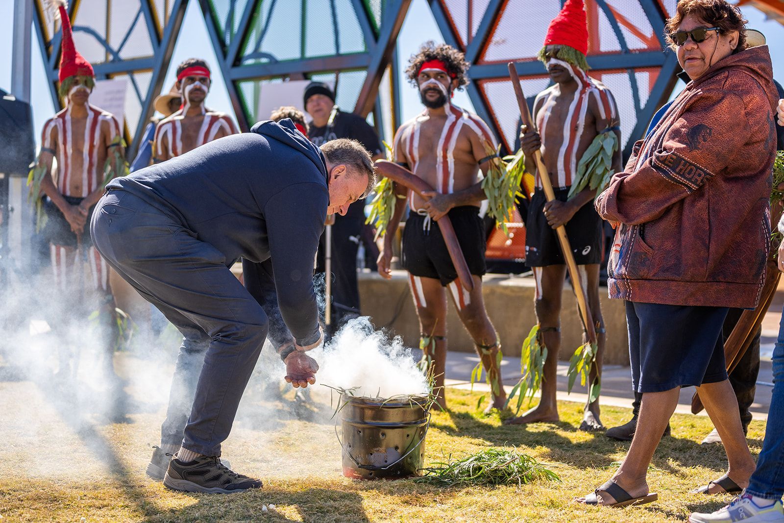 A man is kneeling down in front of a pot with smoke coming out of it.