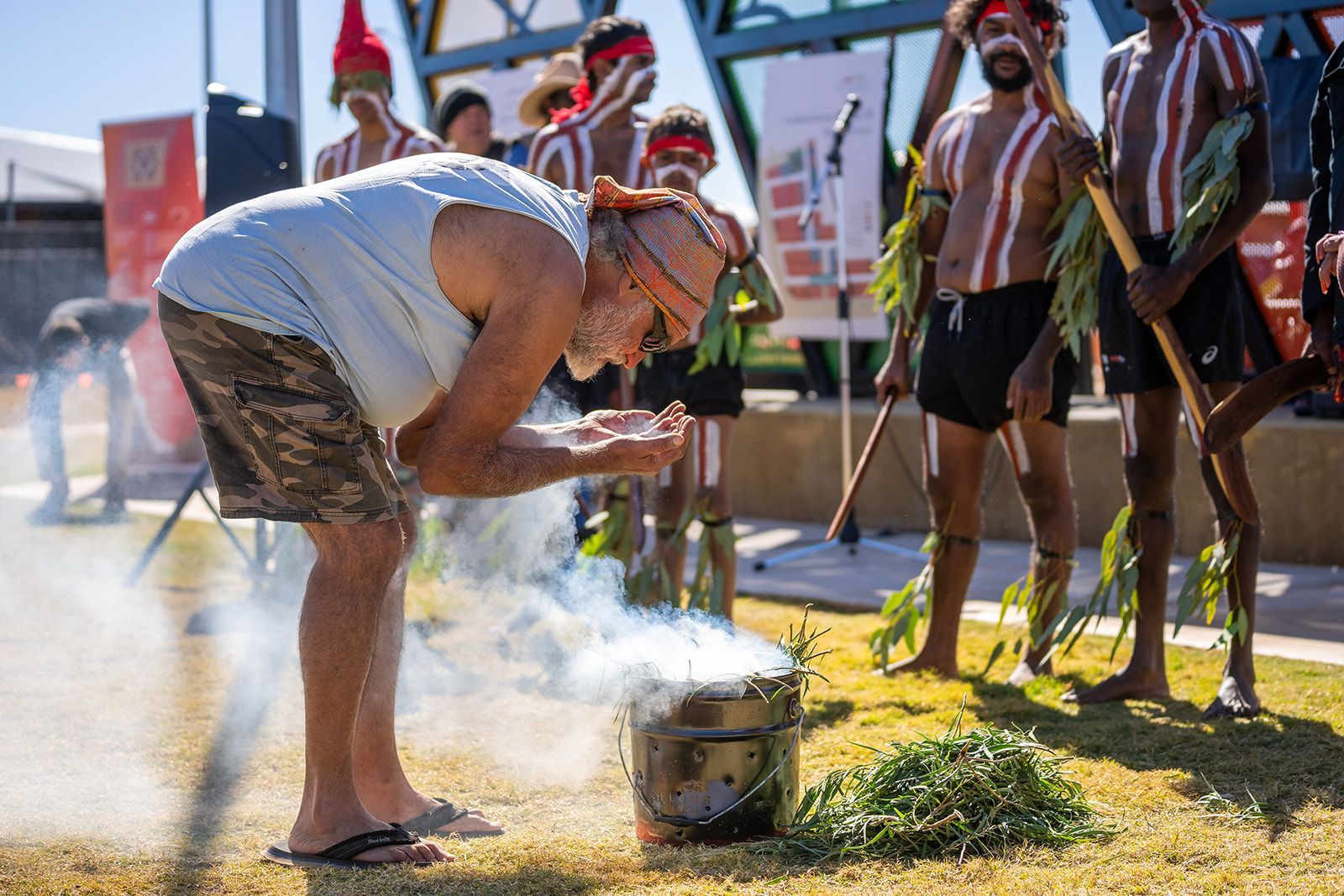 A man is kneeling down in front of a pot with smoke coming out of it.