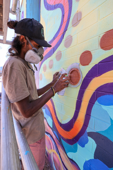 A man wearing a mask is painting a mural on a wall