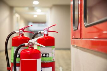 Tres extintores rojos colocados en un pasillo cerca de un gabinete rojo, listos para emergencias.