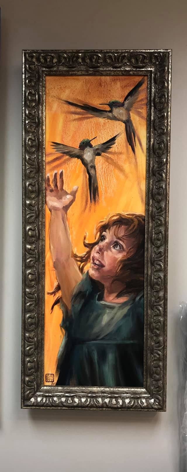 A girl reaches up toward two hummingbirds with a warm orange background.