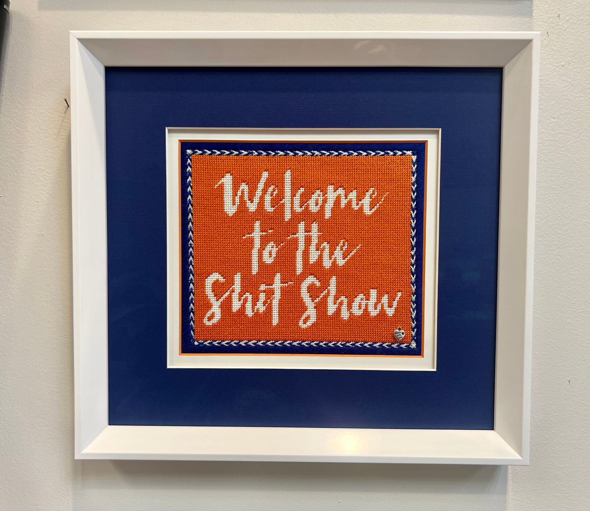 Framed artwork: orange needlepoint reads 