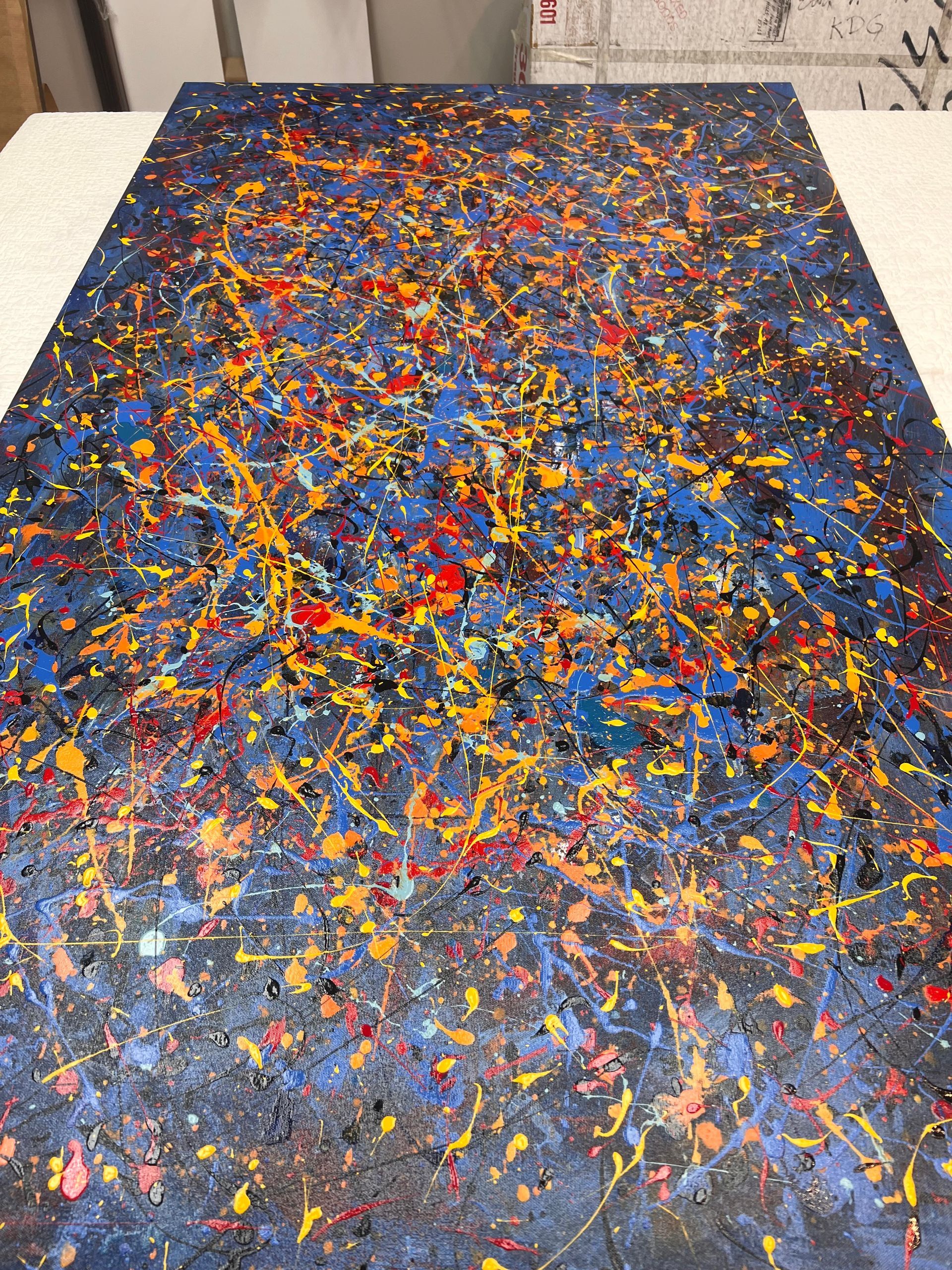 Abstract splatter painting with blue, orange, and red paint on a dark background.