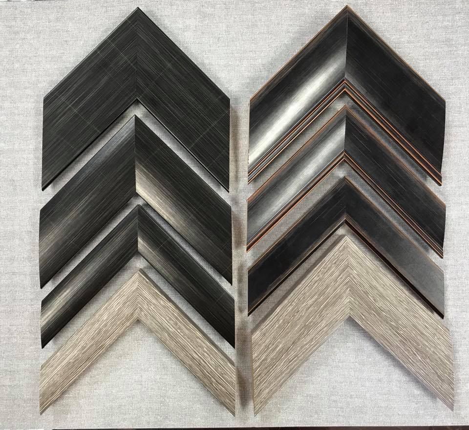 Two assembled picture frame corners in an arrow shape, gray and black brushed metal and light wood-grain colors.