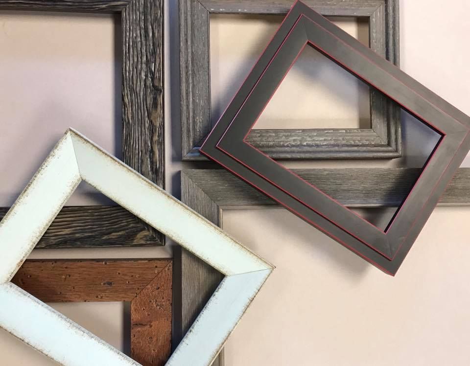 Assorted empty picture frames, various textures and colors, arranged on a neutral wall.