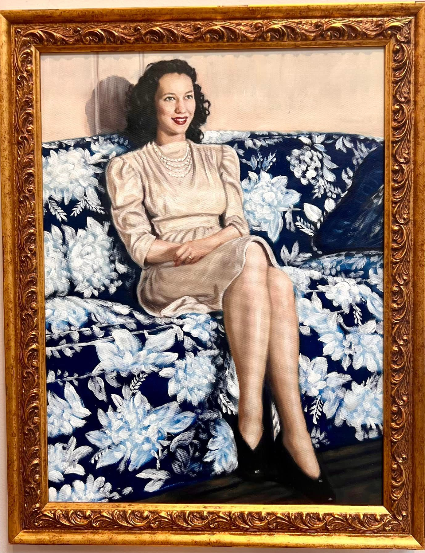 Woman in beige dress sits on floral couch, smiling. Portrait in a gold frame.
