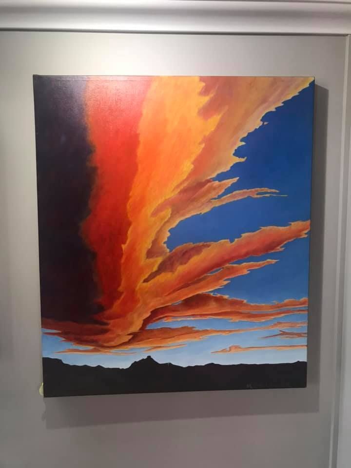 Vivid painting of a fiery orange and red sunset, against a blue sky, over a silhouetted mountain range.