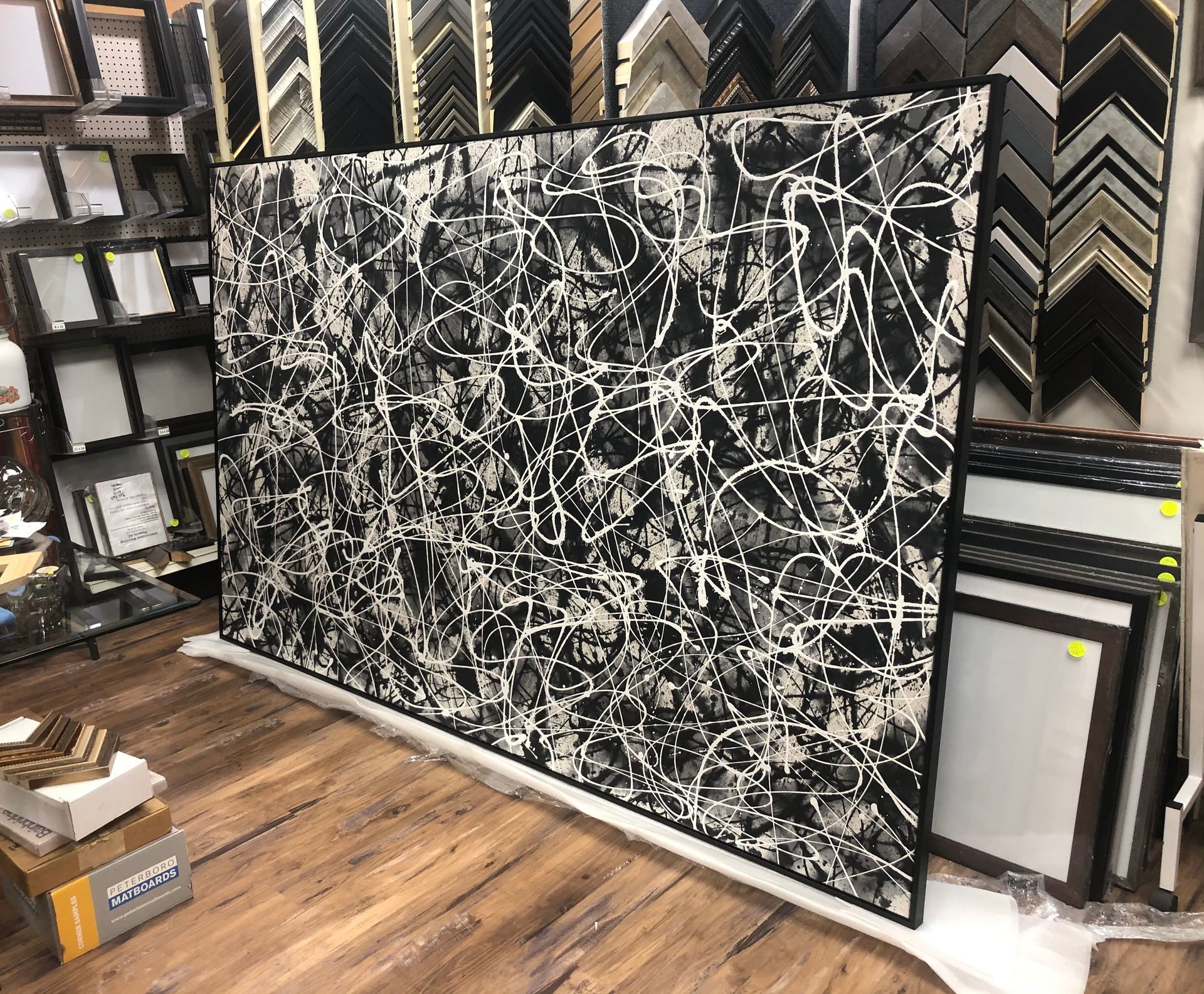 Large black and white abstract painting propped against a wall in a framing shop.