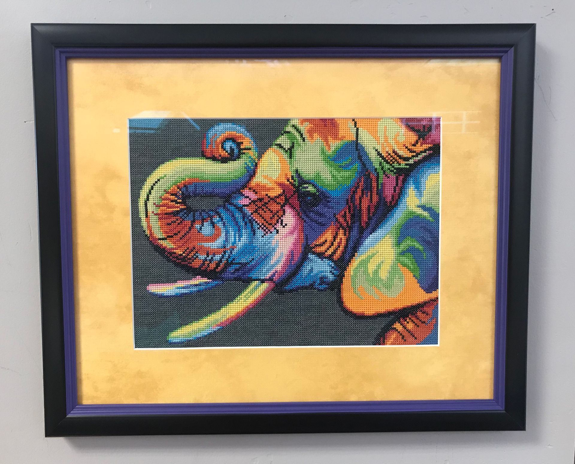 Framed artwork: colorful elephant's head and trunk on a gold mat, surrounded by a black and purple frame.
