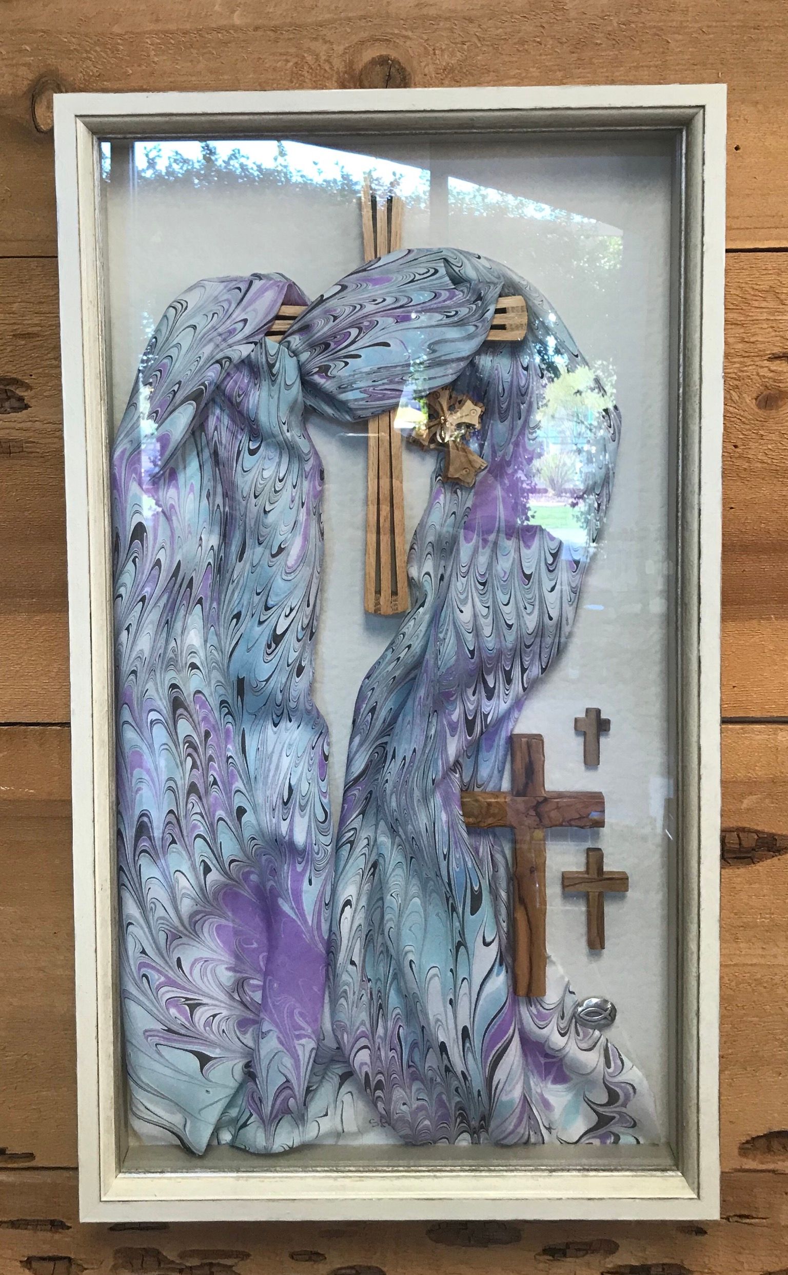 White framed art with draped blue fabric, crosses. Wooden backdrop.