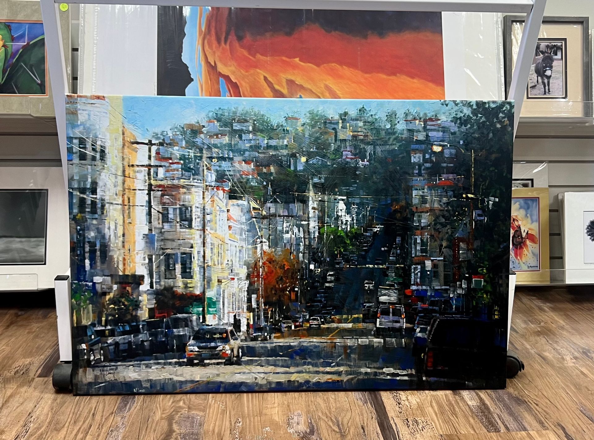 Painting of a city street scene with cars, buildings, and trees, set against a bright sky.
