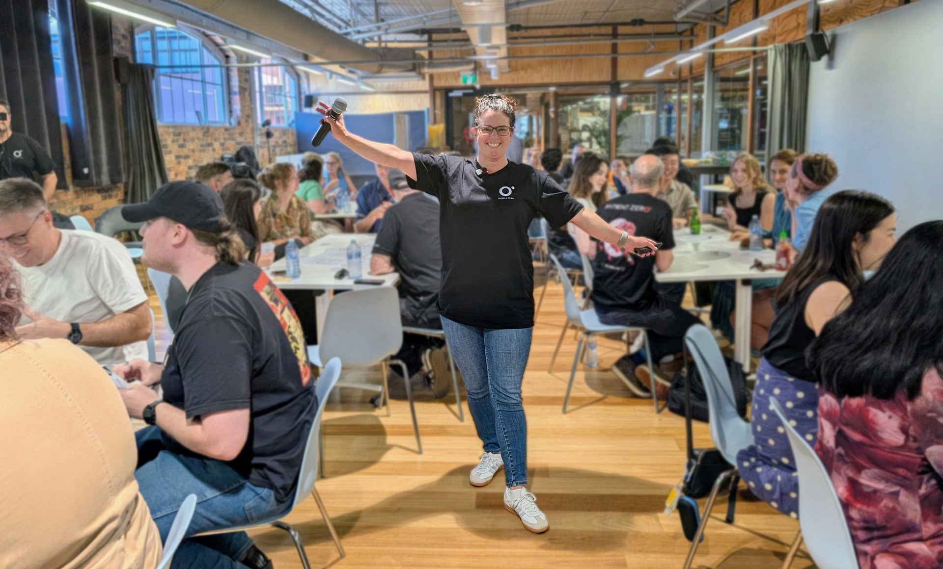 Jacinta Streat from Patient Zero in a room full of people with arms outstretched and a microphone