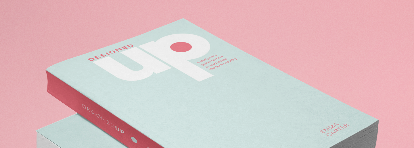Copies of the book DesignedUp are stacked on top of each other on a pink background