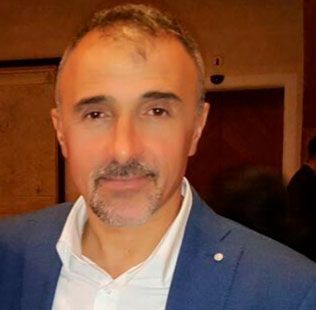 Ein Mann mit Bart trägt einen blauen Anzug und ein weißes Hemd.