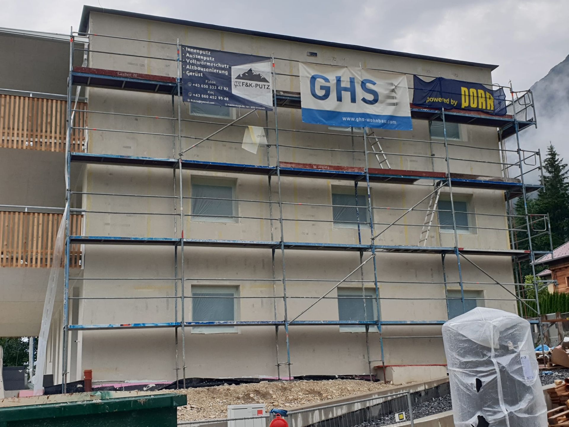 Es wird ein Gebäude mit Gerüst und einem Schild mit der Aufschrift „ghs“ errichtet.