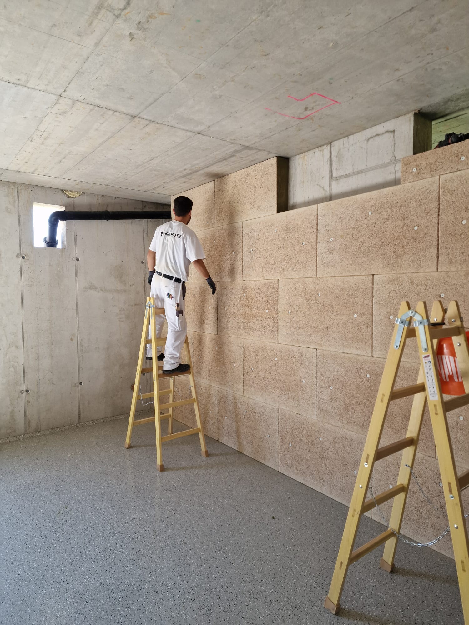 Ein Mann steht auf einer Leiter und streicht eine Wand.