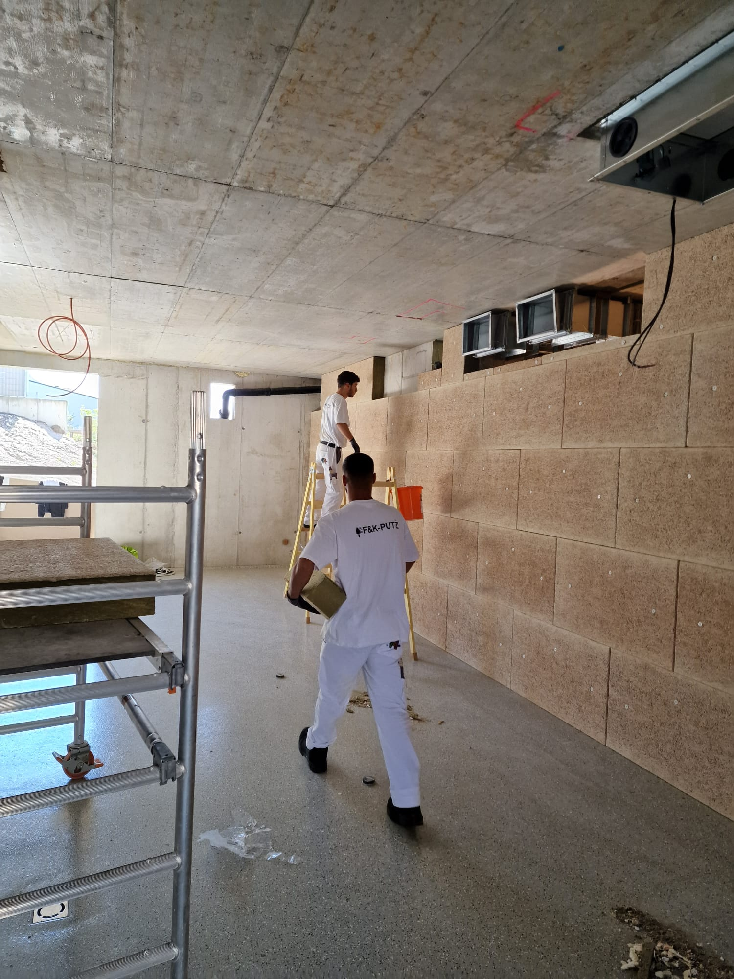 Zwei Männer arbeiten an einer Wand in einem Raum.