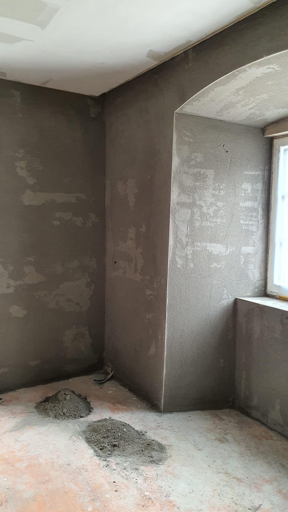 Ein Raum mit Fenster und einer Ecke die verputzt wird.