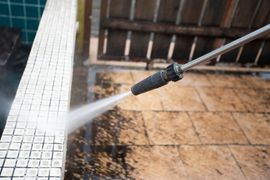 A pressure washer cleaning dirt from a tile pool edge and stone patio.
