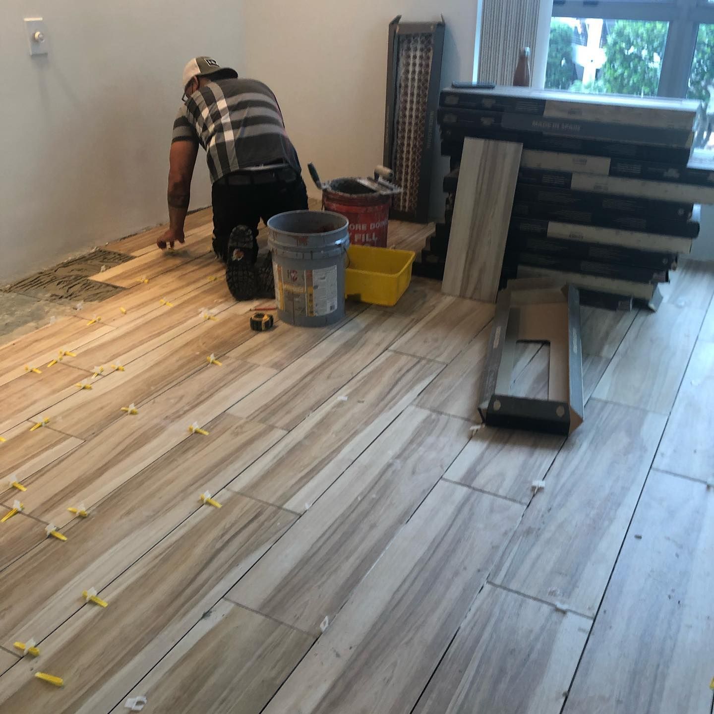 A person installs tile flooring in a room with tools and materials.