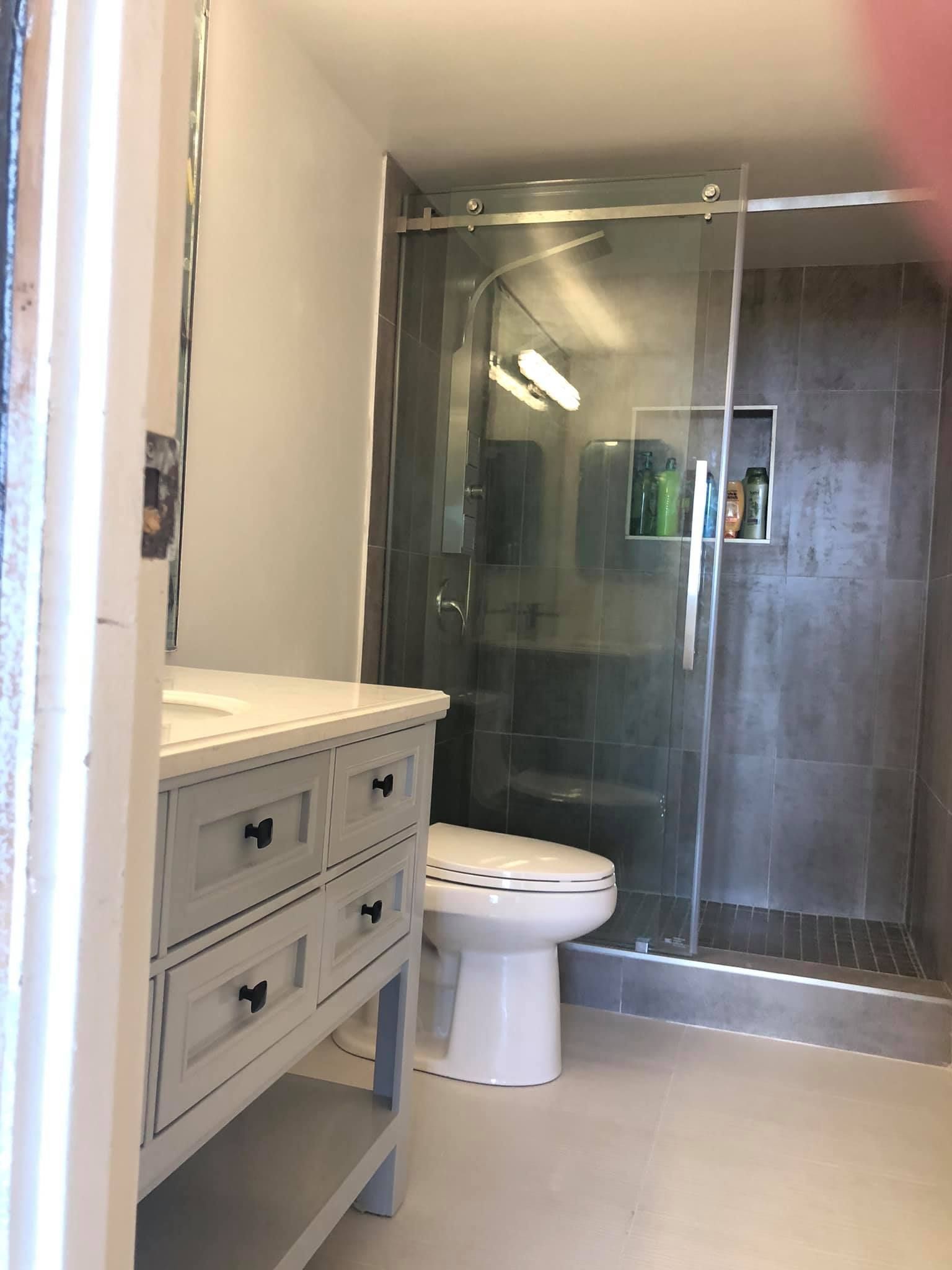 Bathroom with gray tiled shower, white vanity, and toilet.