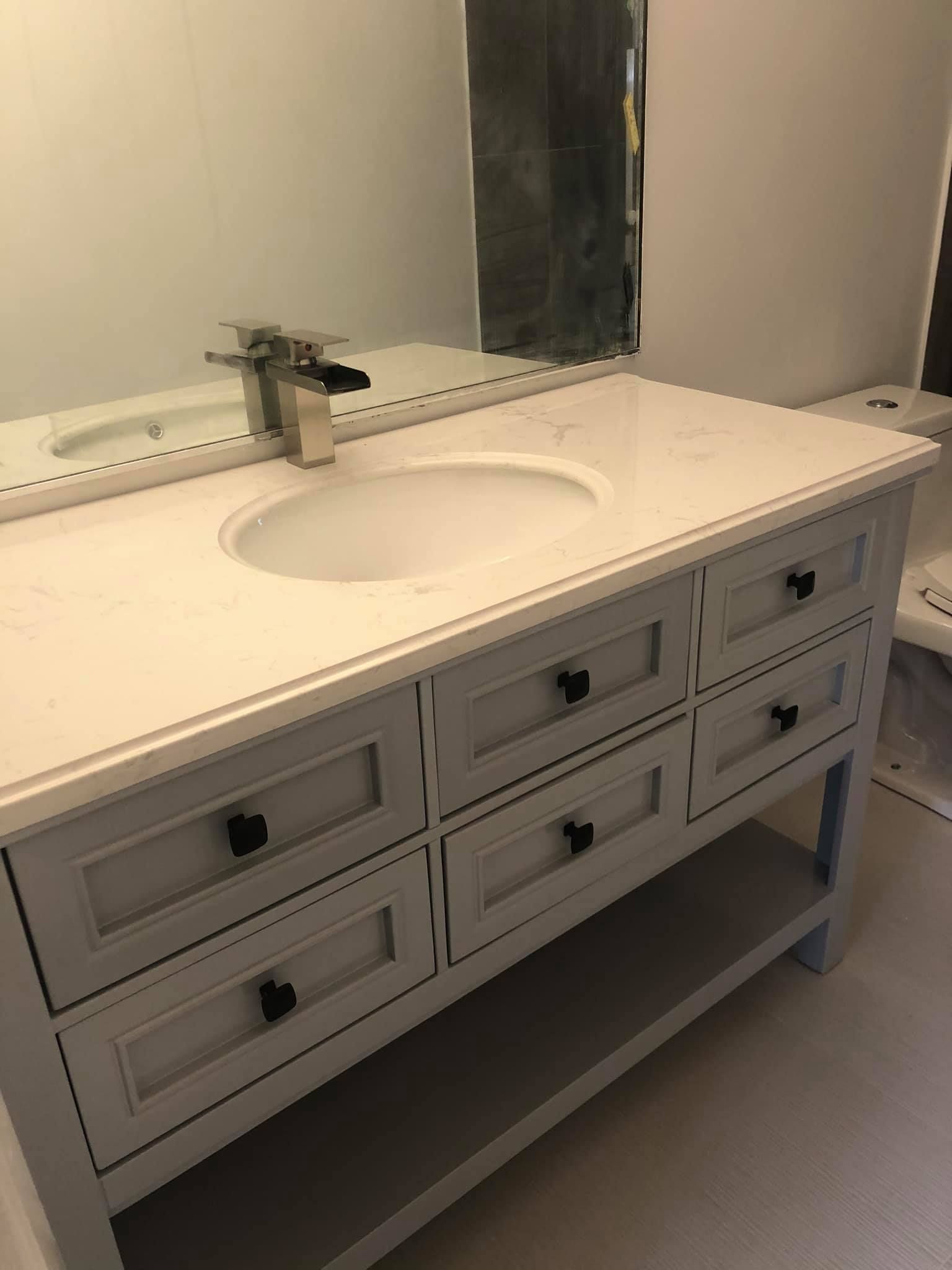 Gray bathroom vanity with quartz countertop, oval sink, and black drawer pulls.