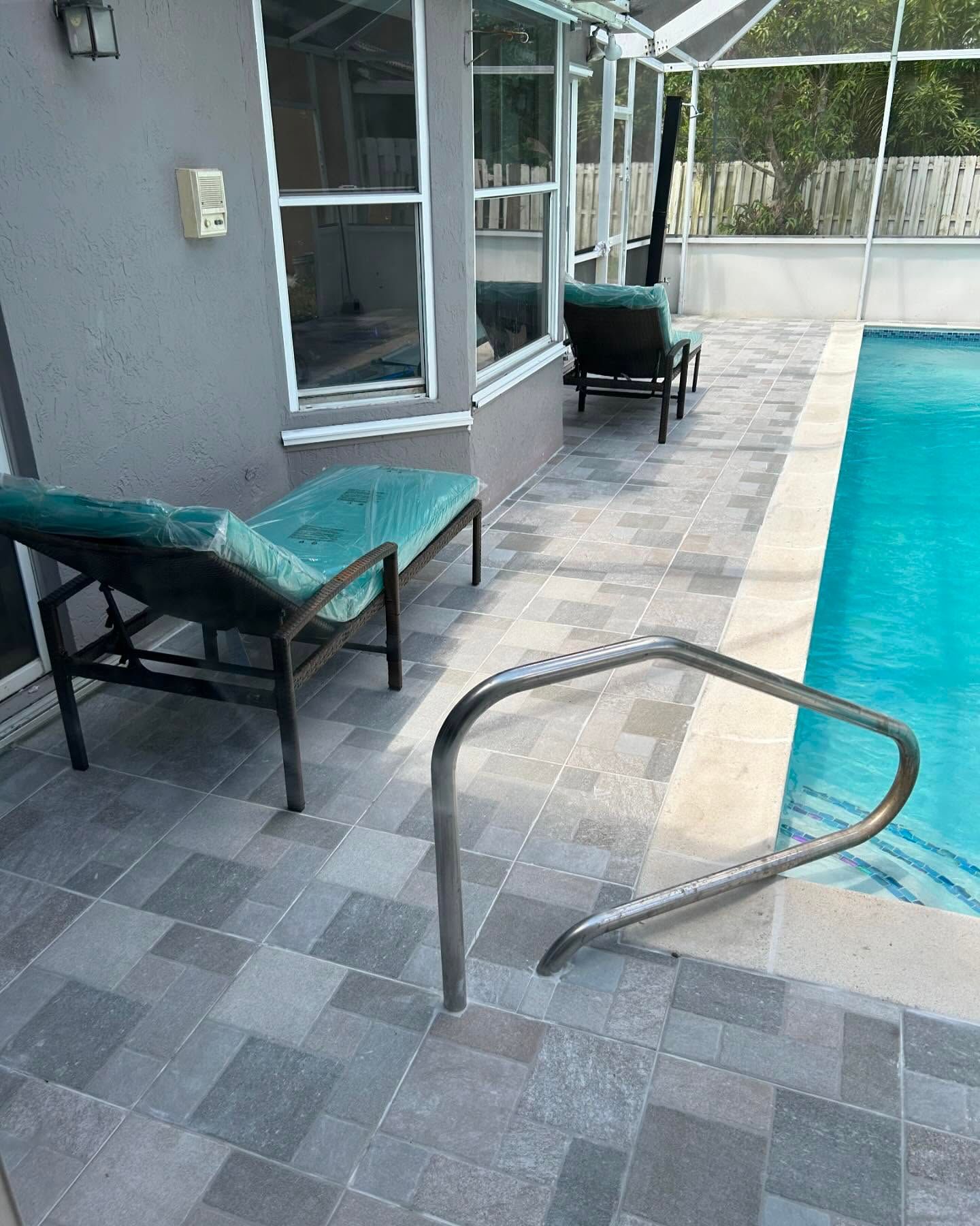 Poolside scene: blue lounge chairs on gray tiled patio, handrail, and pool with clear water.
