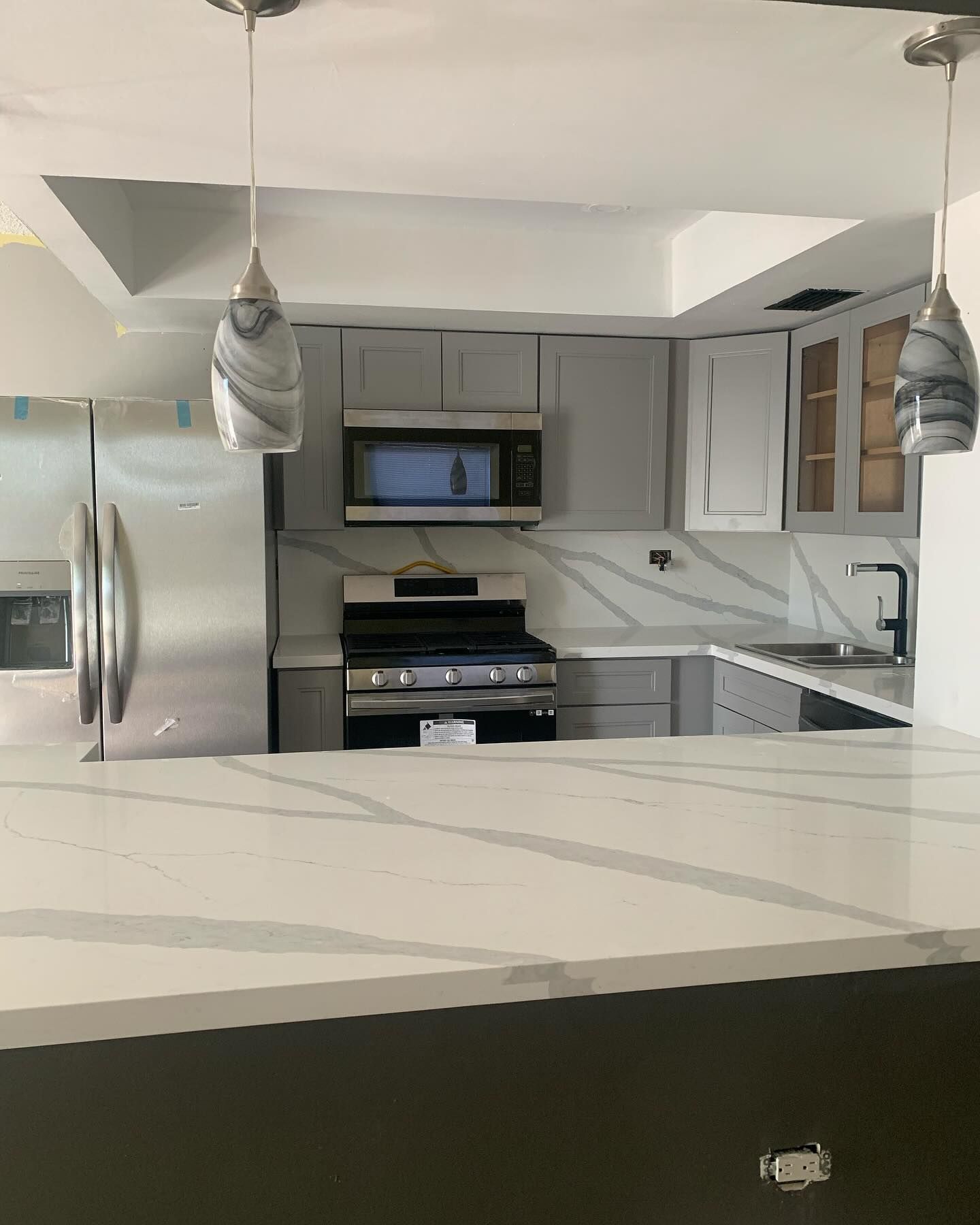 Modern kitchen with gray cabinets, marble countertops, stainless steel appliances, and pendant lights.