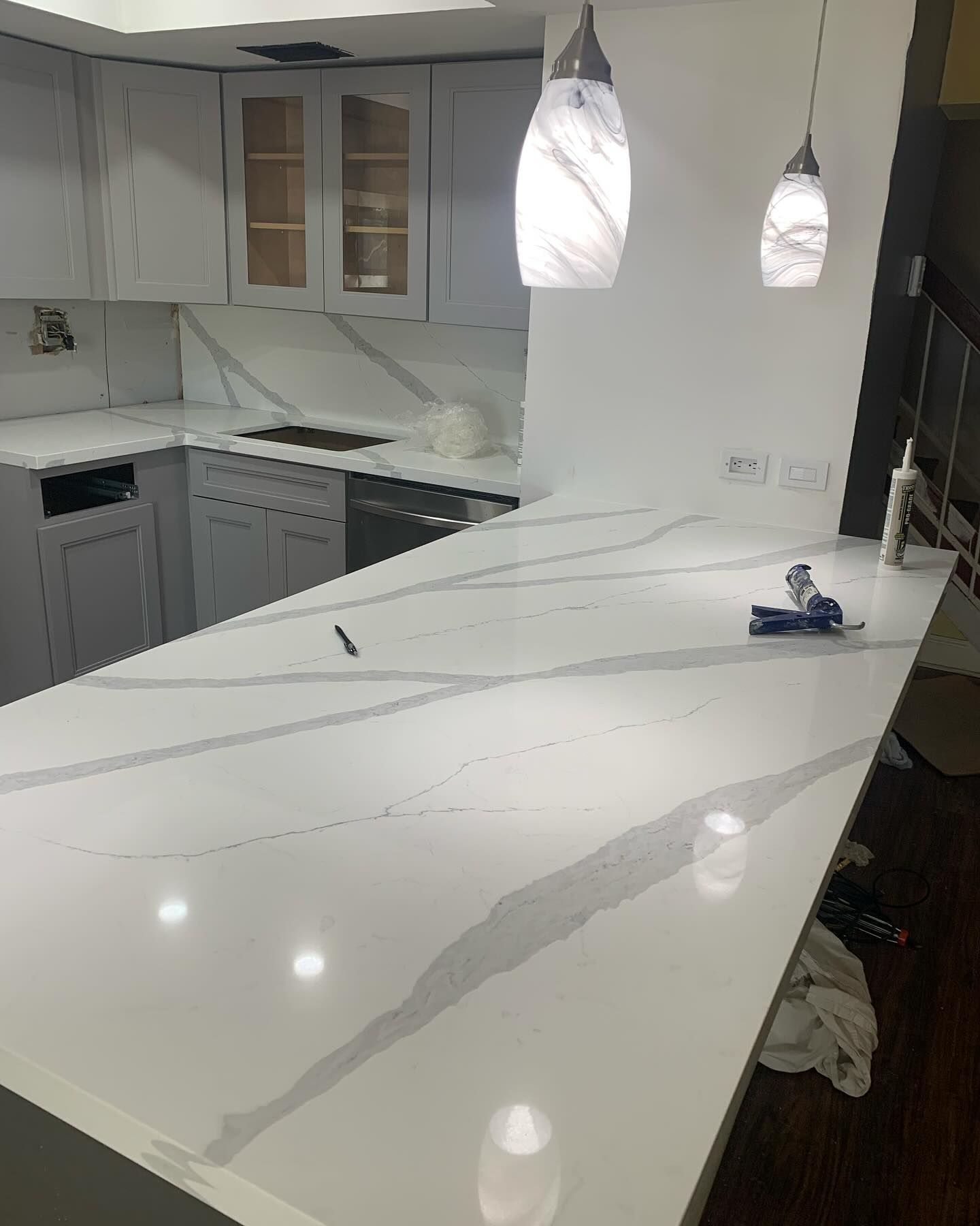 White kitchen countertop with gray veining; pendant lights.