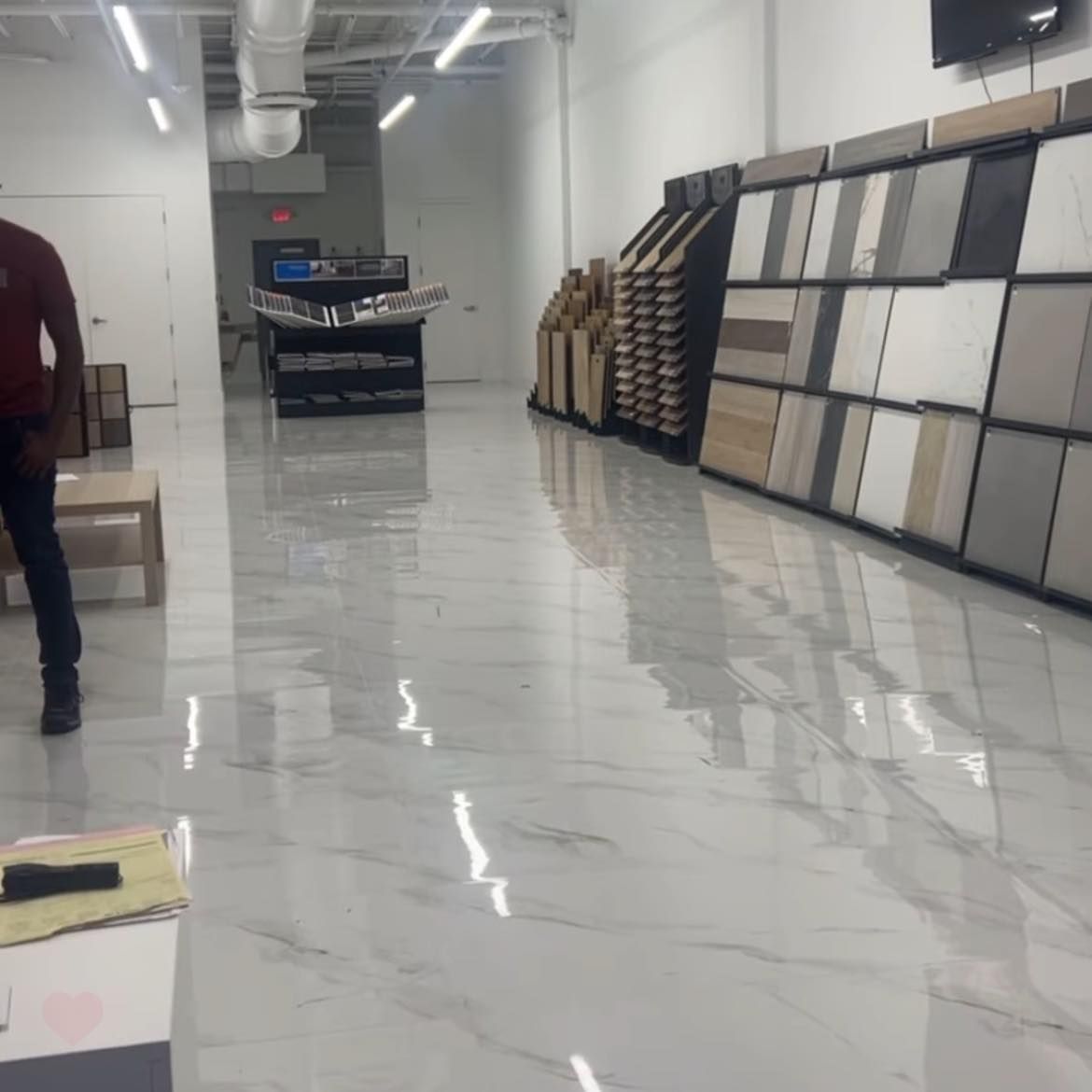 Bright showroom with shiny white floor, tile samples, and a person walking.