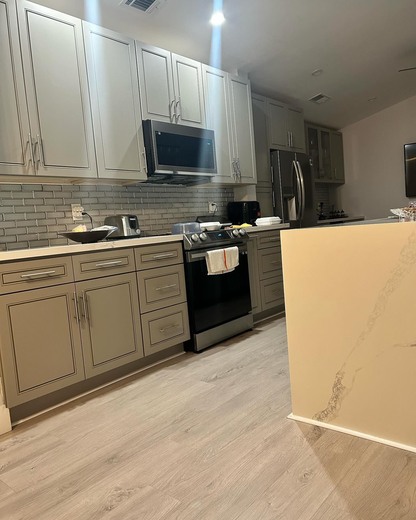 Kitchen with gray cabinets, appliances, backsplash, and light wood-look flooring.