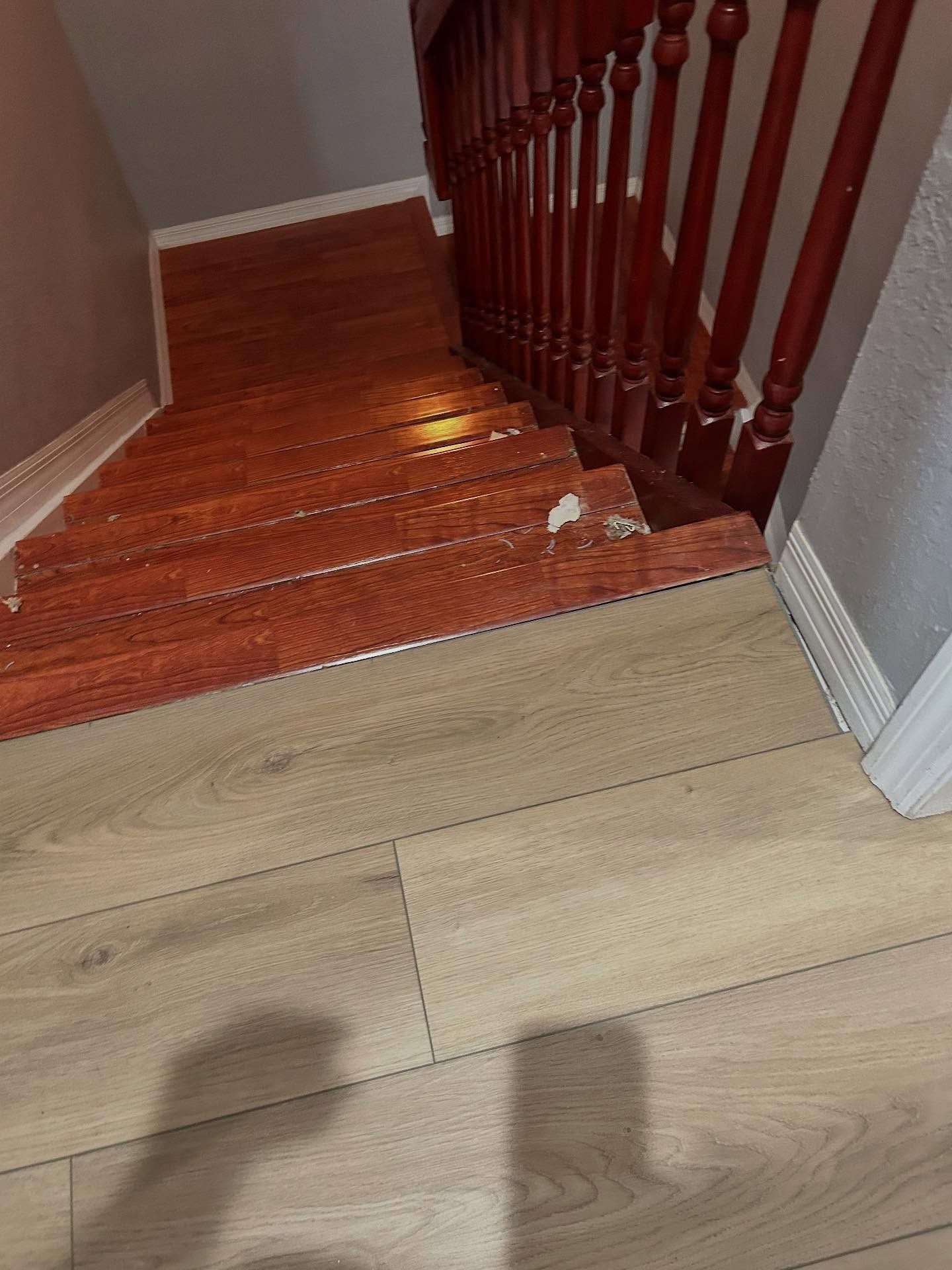 Staircase with red-brown wood steps leading down, transitioning to light-colored flooring. Red railing on the right.
