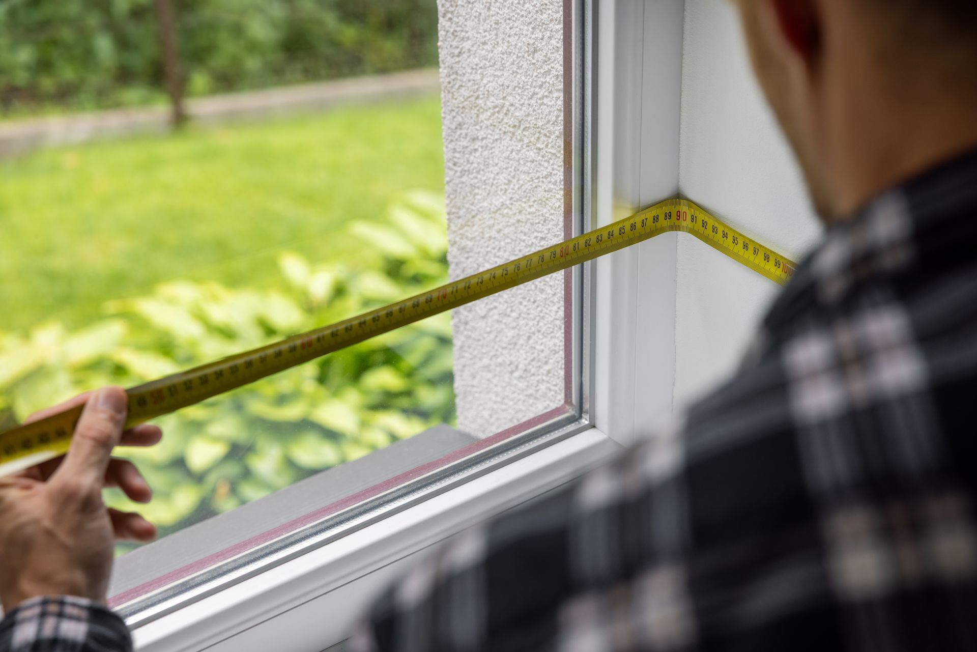 Person measuring window frame with tape measure during home window replacement work.