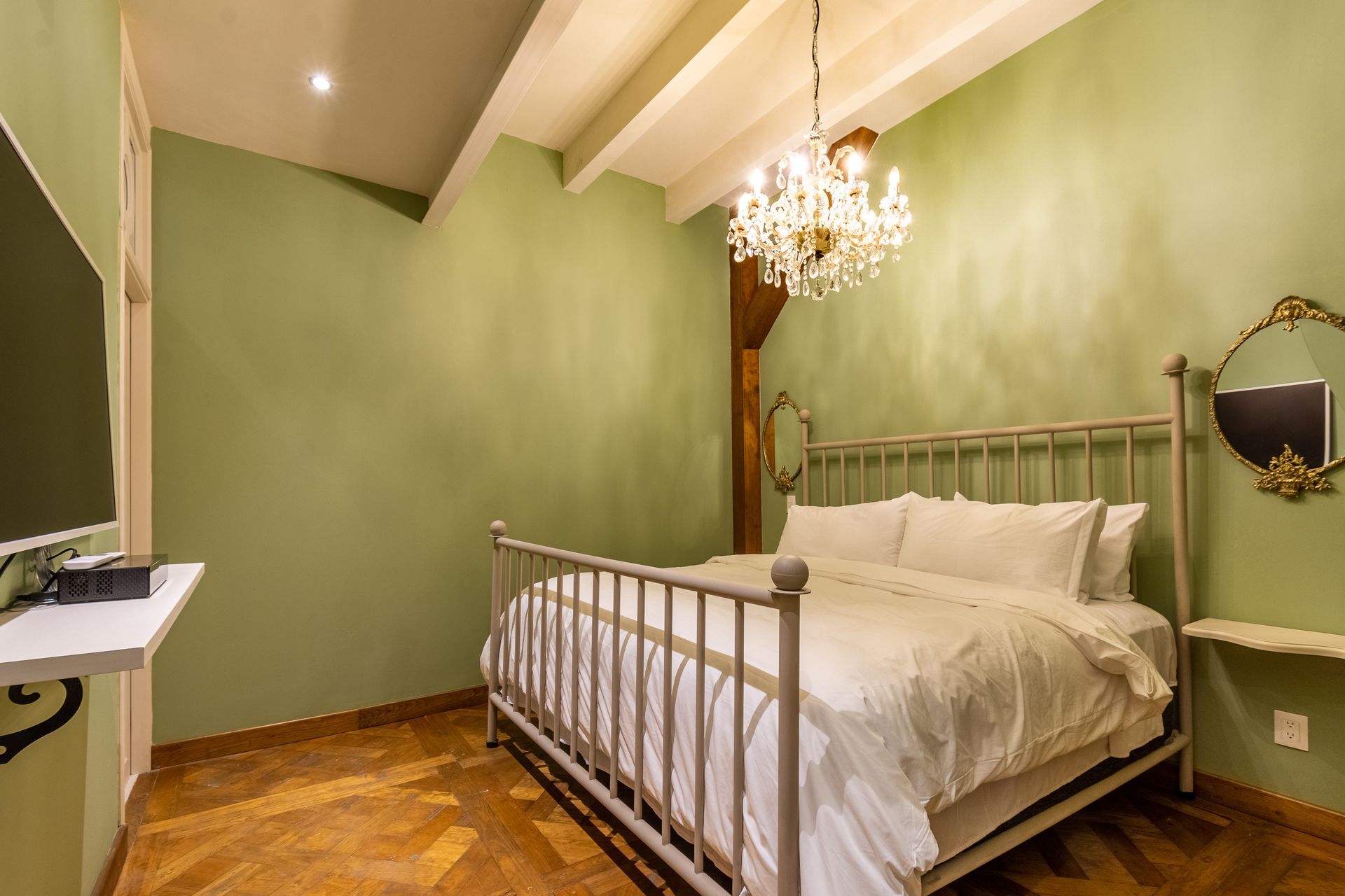 Un dormitorio con cama, televisión, espejo y lámpara de araña.