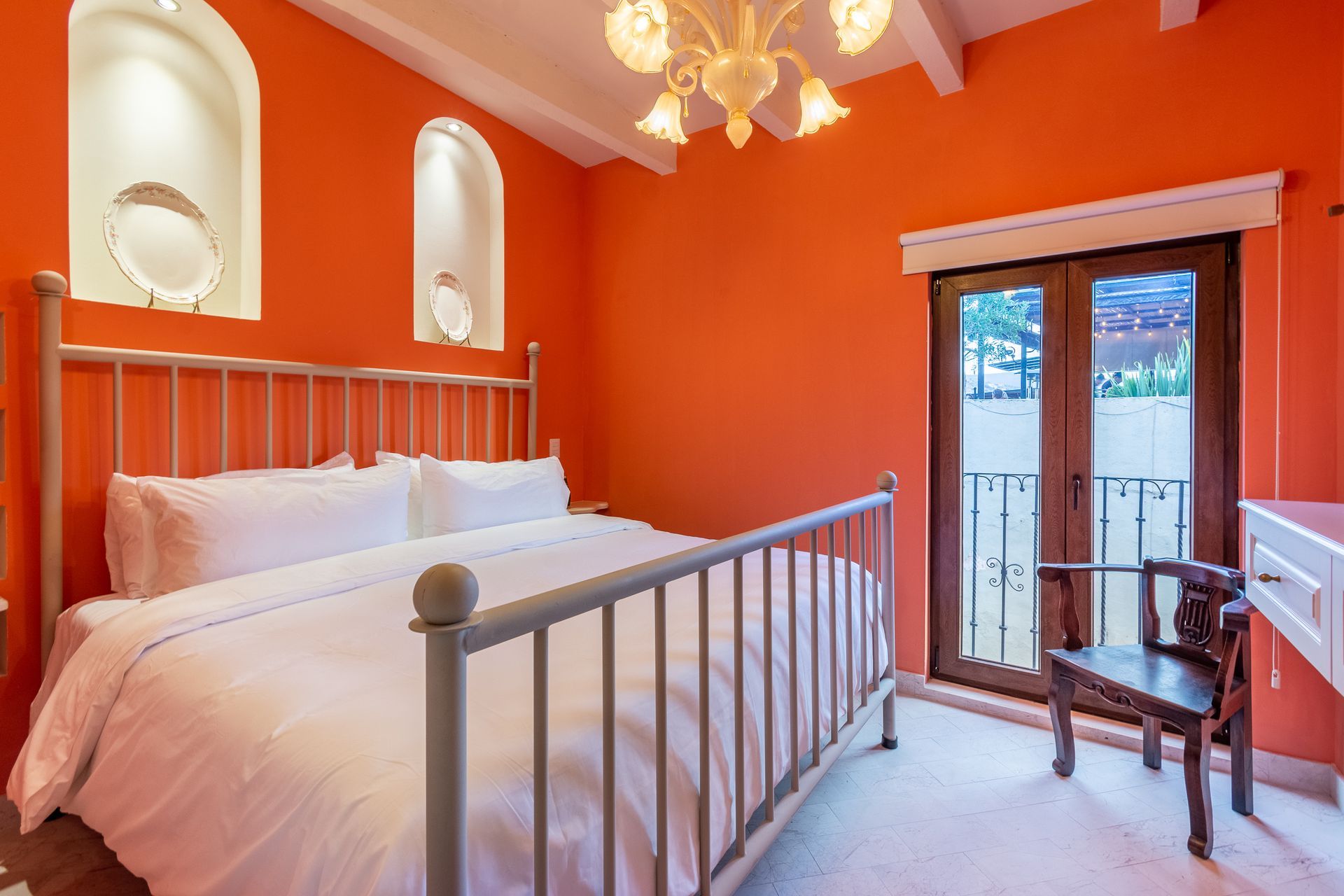 Un dormitorio con paredes naranjas y una cama con sábanas blancas.