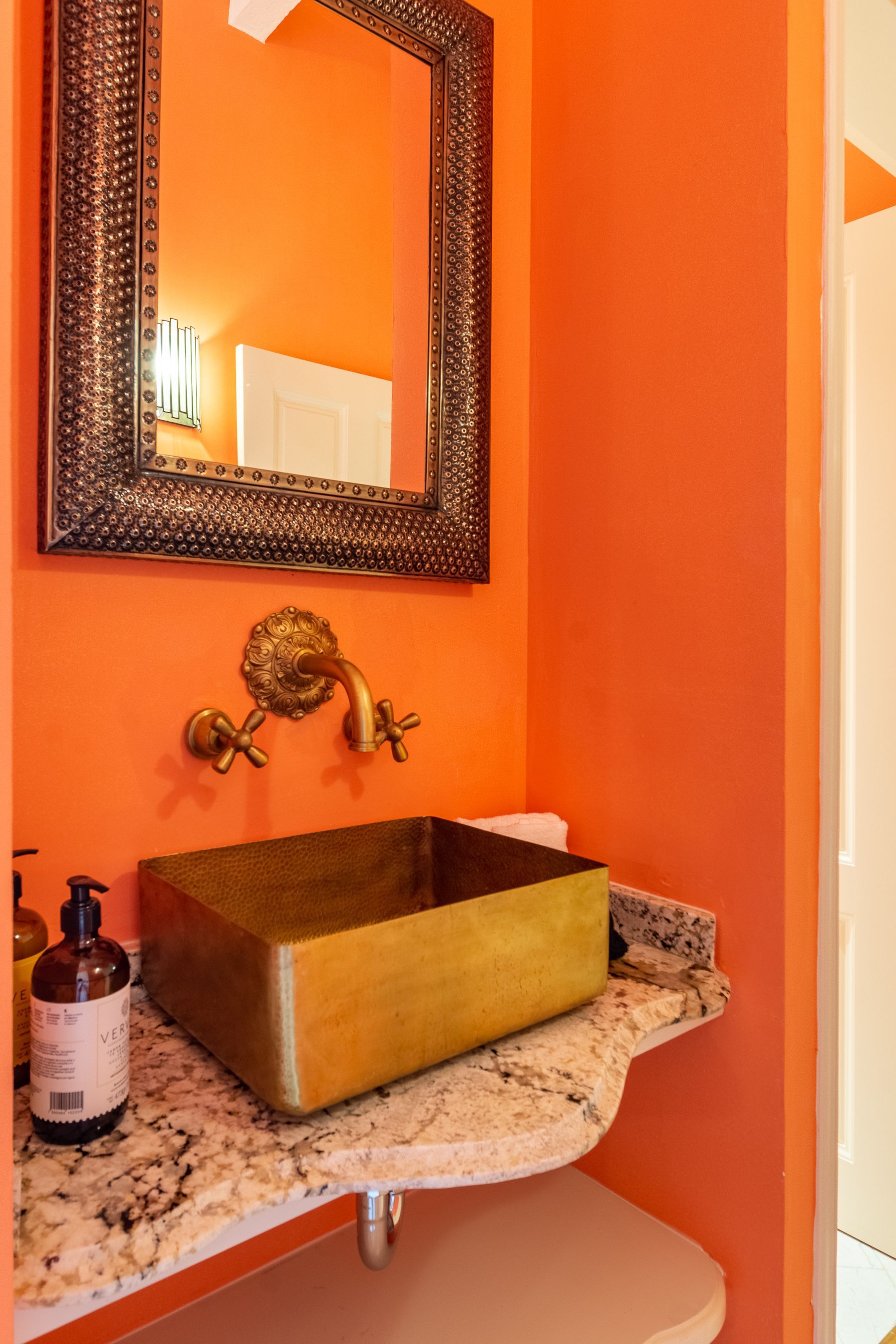 Un baño con paredes naranjas, lavabo y espejo.