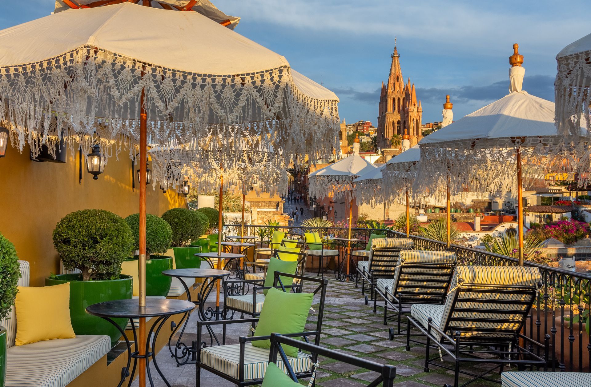 Un patio con mesas y sillas bajo sombrillas con una ciudad al fondo.