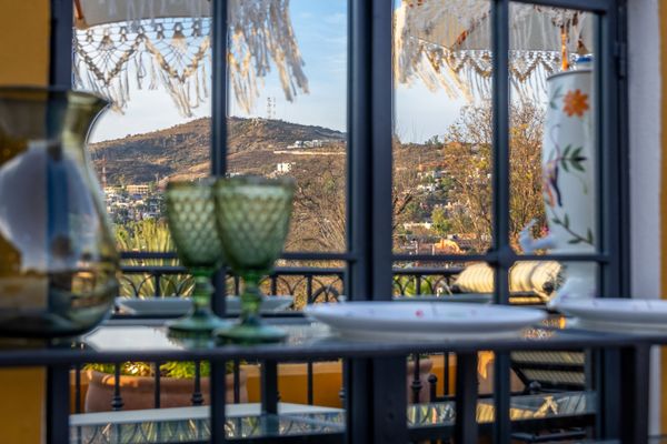 Una mesa con platos y copas de vino frente a una ventana con vista a las montañas.