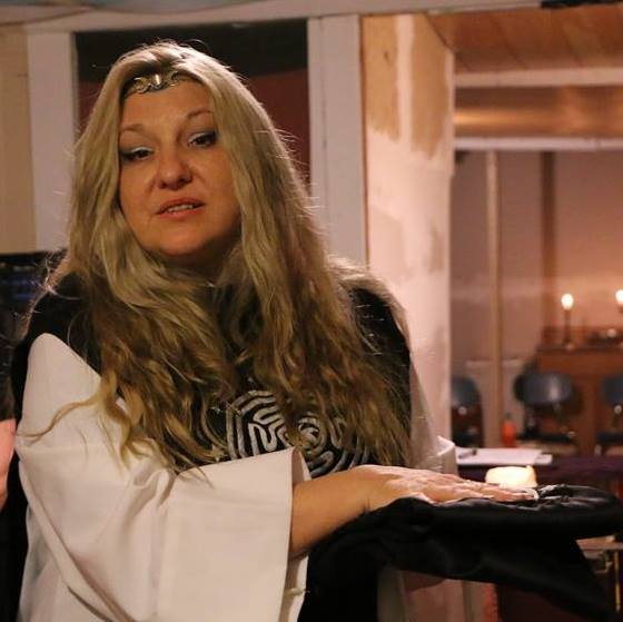 A woman with long blonde hair is wearing a Hekate's Labyrinth shirt, Belladonna LaVeau.