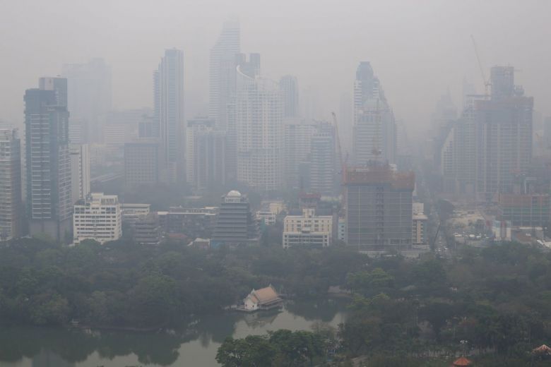 A city skyline covered in smog with a lake in the foreground.