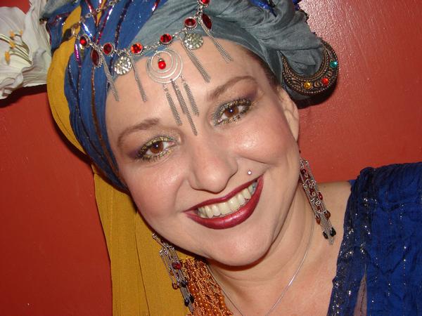 A woman wearing a turban and earrings smiles for the camera, Belladonna LaVeau.