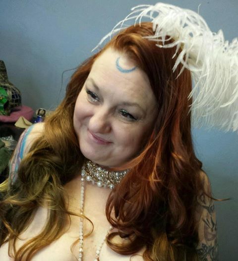 A woman with red hair and a white feather on her head, Belladonna LaVeau as Aprhodite.