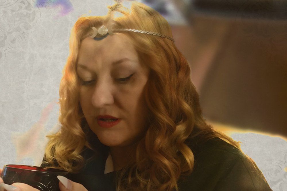 A woman with red hair is wearing a headband and holding a cup, Belladonna LaVeau.