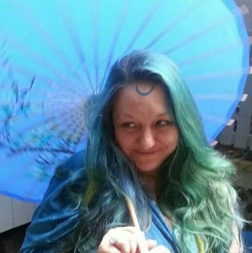 A woman with green hair is holding a blue umbrella, Belladonna LaVeau.